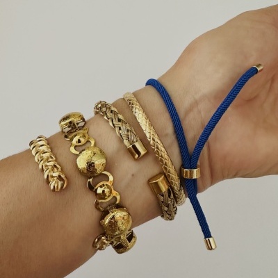 Pulseiras douradas e azul com texturas variadas no pulso de uma mão