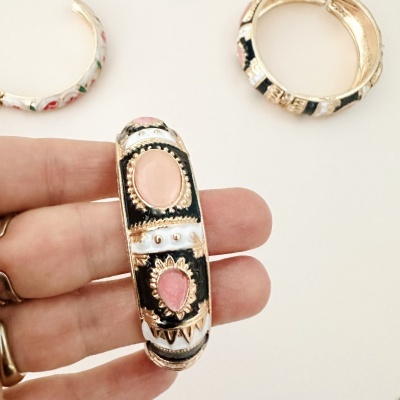 Braceletes esmaltados coloridos com detalhes dourados em relevo, um segurado por mão.