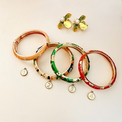 Quatro pulseiras coloridas metálicas com medalhas numeradas e brincos de abelha com pérola