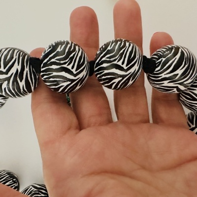 Colar com contas redondas padrão zebra segurado por mão