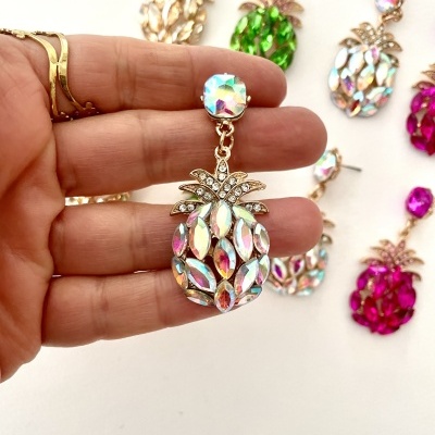 Brinco em forma de ananás com pedras coloridas, base dourada, mostrado junto a outros brincos semelhantes sobre fundo branco.