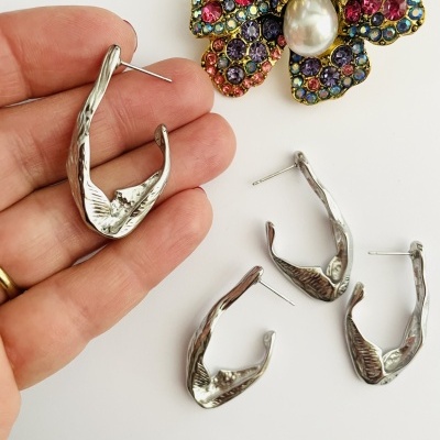 Brincos de argola prateados com textura ondulada ao lado de broche florido colorido