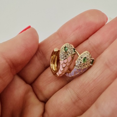 Brincos dourados com esmalte rosa e lilás e pedras verdes em mão com unhas vermelhas