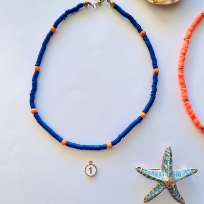 Colar azul com contas laranja e pendente número 1, sobre fundo branco com concha dourada e estrela do mar azul