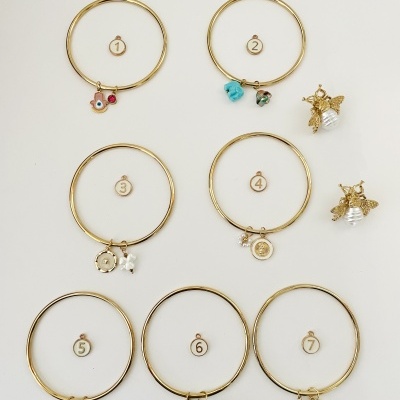 Sete brincos de argola dourada com diferentes pingentes coloridos num fundo branco