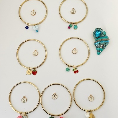 Sete pulseiras douradas com pendentes coloridos e um objeto azul em forma de concha