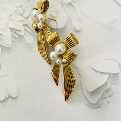 Brincos dourados em forma de laço com pérolas sobre fundo floral branco