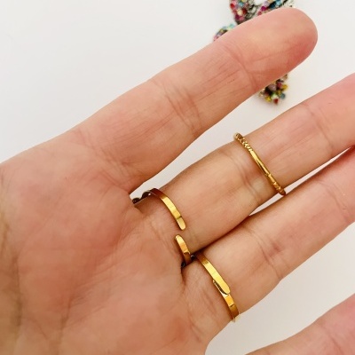 Mão com três anéis dourados finos em fundo branco com decoração colorida desfocada