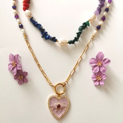 Colares coloridos e dourado com pendente de coração, brincos florais lilás sobre fundo branco.