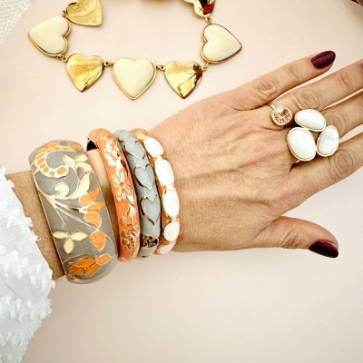 Pulseiras e anéis decorativos em tons neutros e alaranjados com padrões florais e corações, mão feminina com unhas roxas