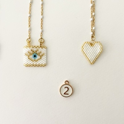 Dois colares dourados com pendentes de miçangas, olho azul quadrado e coração branco, fundo branco, medalha com '2'