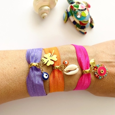 Pulseiras coloridas com pendentes dourados em braço com fundo branco e decorações ao fundo