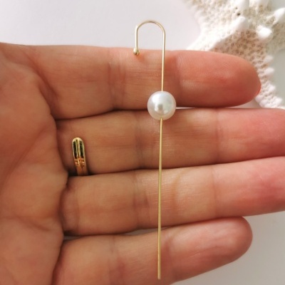 Pendentes dourados com pérola branca numa mão e estrela do mar ao fundo