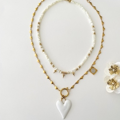 Dois colares, um com contas brancas e detalhes dourados, outro dourado com pendente coração branco, sobre fundo branco com flores decorativas.