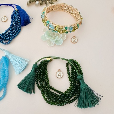 Pulseiras coloridas em azul, dourado e verde com contas e franjas sobre fundo claro, marcadas com números.
