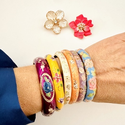 Pulseiras florais coloridas no pulso e duas presilhas de cabelo florais num fundo branco