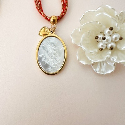 Colar com pendente oval dourado translúcido e cordão vermelho com flor branca decorativa.