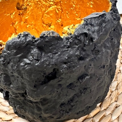 Vaso decorativo preto com interior dourado sobre esteira de palha