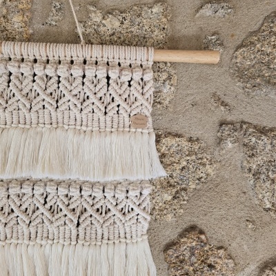 Têxtil decorativo em macramé creme com franjas numa parede de pedra