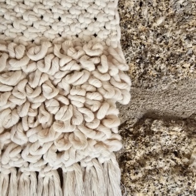 Tecido artesanal branco com textura volumosa e etiqueta Marra Marrone sobre superfície rugosa