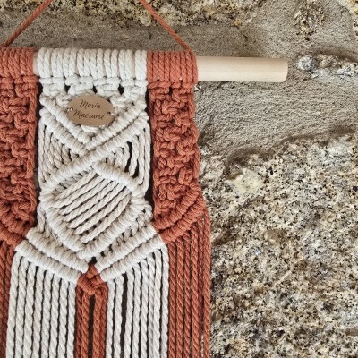 Tapete decorativo em macramê bege e castanho pendurado na parede de pedra