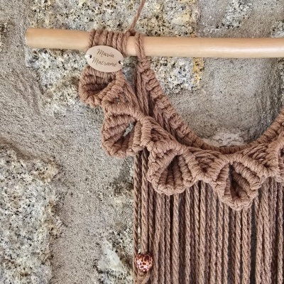 Decoração de macramê castanho com varão de madeira na parede de pedra