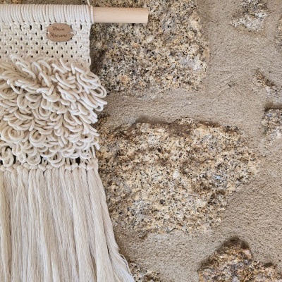 Painel decorativo em macramé bege claro pendurado em parede de pedra rústica