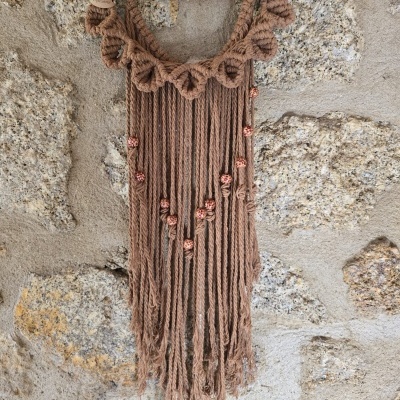 Pendurar decorativo artesanal em macramé castanho com madeira numa parede de pedra