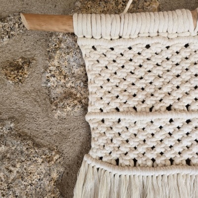 Tapete decorativo em macramé branco pendurado numa parede de pedra