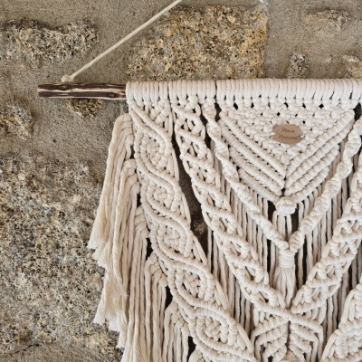 Tapeçaria de macramé de algodão cru pendurada numa parede de pedra