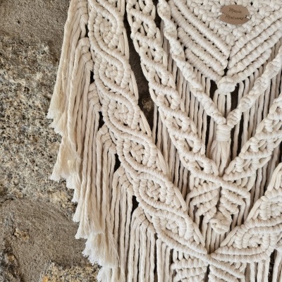 Tapete decorativo macramé em algodão cru, textura entrançada, pendurado numa parede de pedra