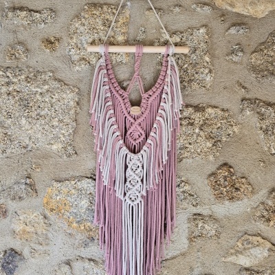Macramé decorativo rosa e creme pendurado numa parede de pedra