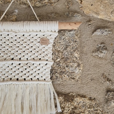 Tapete macramé branco pendurado em parede de pedra