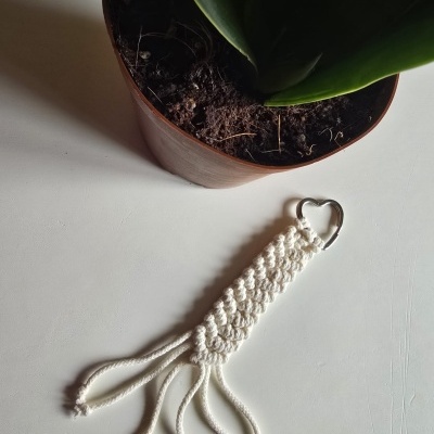 Chaveiro de corda branca trançada com argola em forma de coração ao lado de vaso com planta