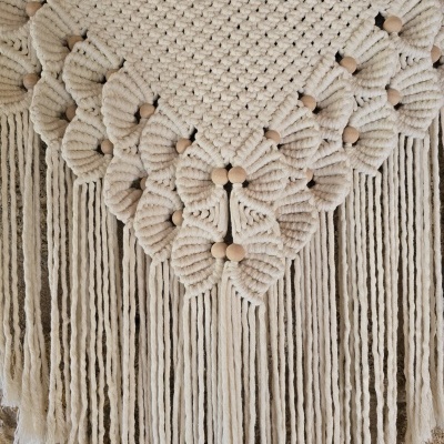 Tapeçaria macramé em algodão cru com franjas e acessórios de madeira em fundo neutro