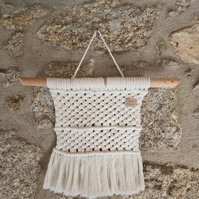 Tapeçaria de parede em macramé branca com franjas pendurada na parede de pedra