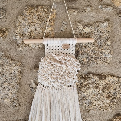Tapeçaria decorativa em macramé creme pendurada em parede de pedra