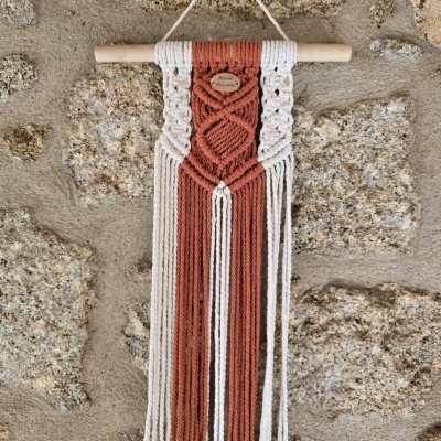 Tapeçaria decorativa em algodão branco e castanho pendurada numa parede de pedra