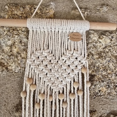 Tapeçaria de macramé com coração em contas de madeira pendurada numa parede de pedra
