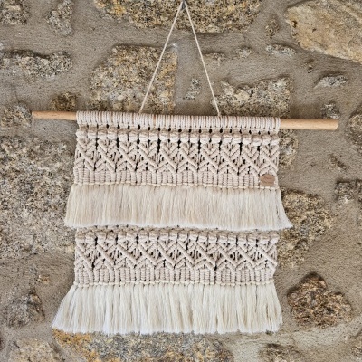 Painel decorativo em macramé cru com franjas pendurado numa parede de pedra