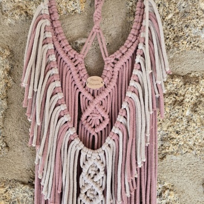Pendente decorativo de macramé rosa e bege numa parede de pedra
