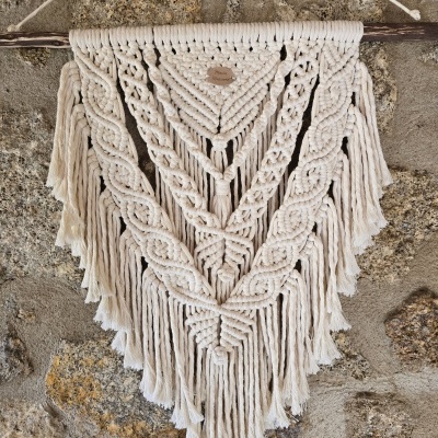 Tapeçaria de macramé bege com franjas pendurada numa parede de pedra