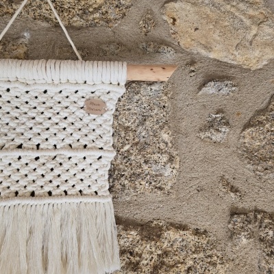 Tapeçaria em macramé branca pendurada numa parede de pedra