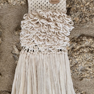 Tapete pendurado de macramé cru com etiqueta em madeira e parede de pedra