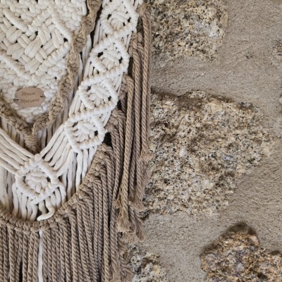 Pendurador de parede em macramé creme e castanho numa parede de pedra