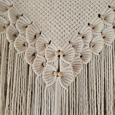 Decoração em macramê creme com franjas e flores trançadas com contas de madeira.