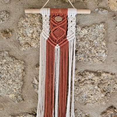 Tapeçaria de macramé branca e terracota pendurada numa parede de pedra