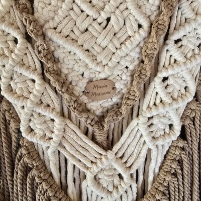 Macramé com padrões geométricos em tons bege e castanho com etiqueta 'Maria Macramé'.