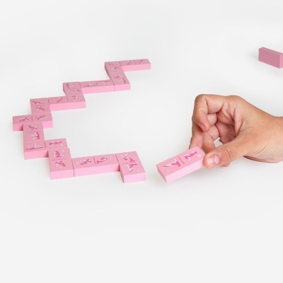 Peças de dominó rosa com desenhos em relevo e mão a segurar uma peça sobre fundo branco