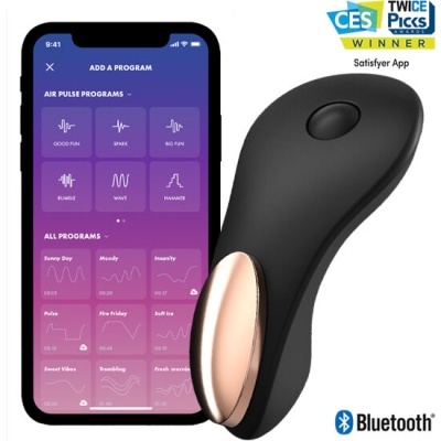 Dispositivo preto com detalhe dourado ao lado de telemóvel com app Satisfyer em fundo branco